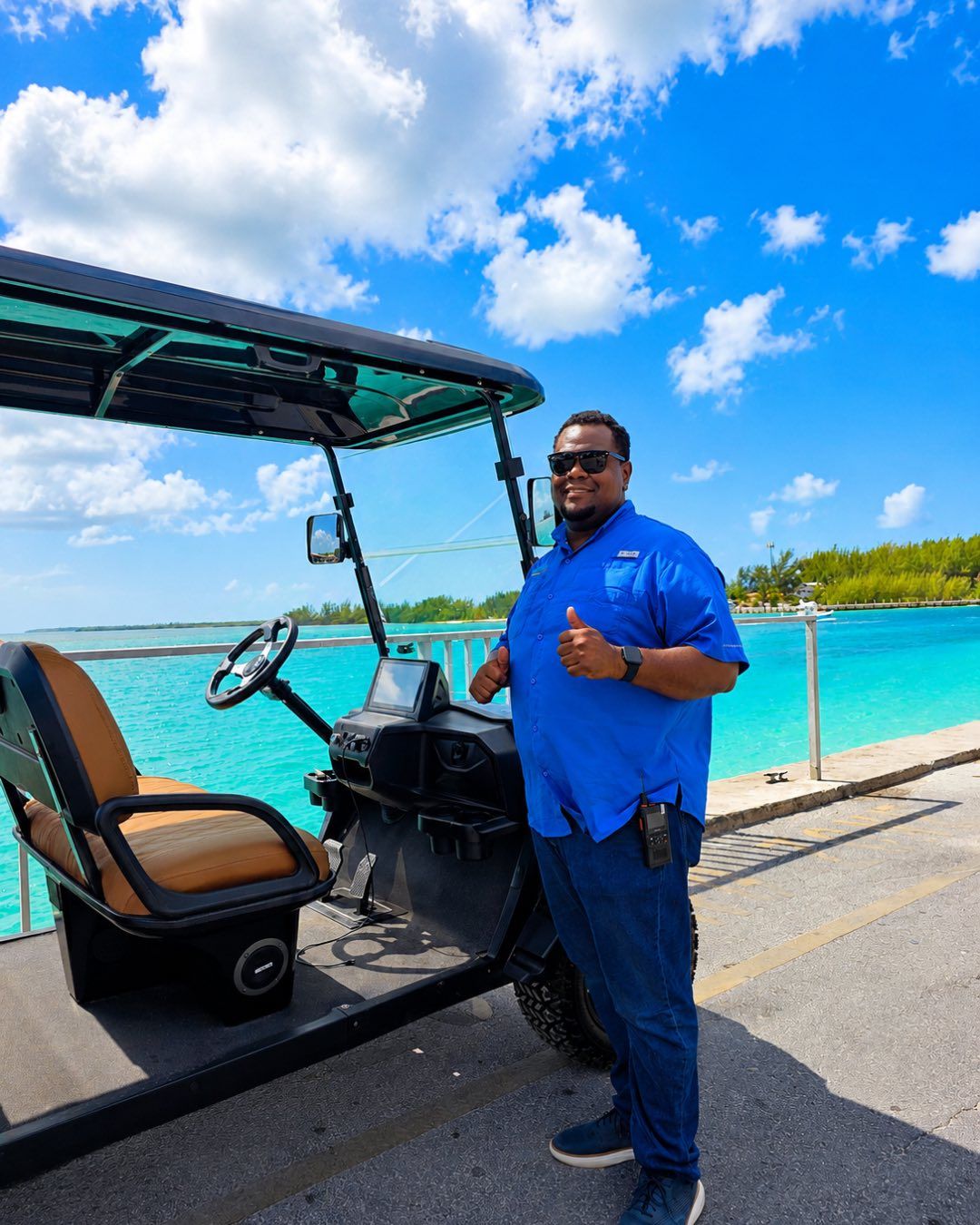 A BMB host in a blue shirt beside a golf cart, with the harbor behind him.
