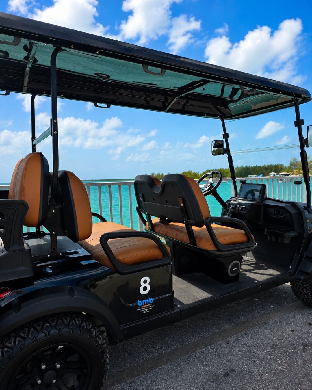 A six-passenger golf cart parked on an island road beside turquoise water.
