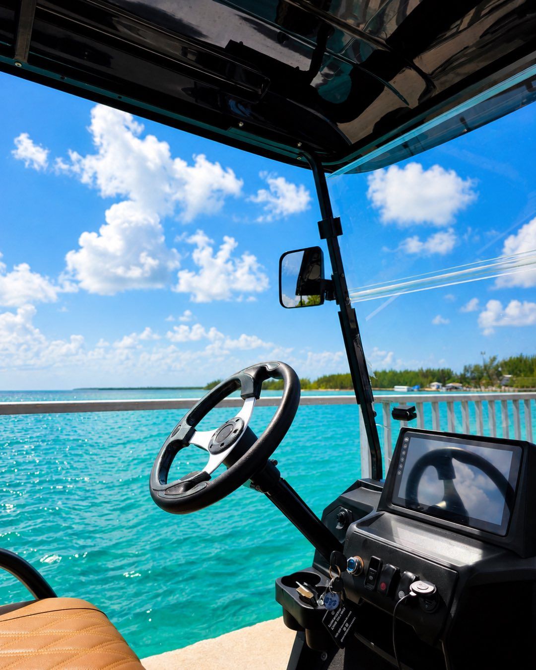 The view from a golf cart’s driver seat, looking out over turquoise water.