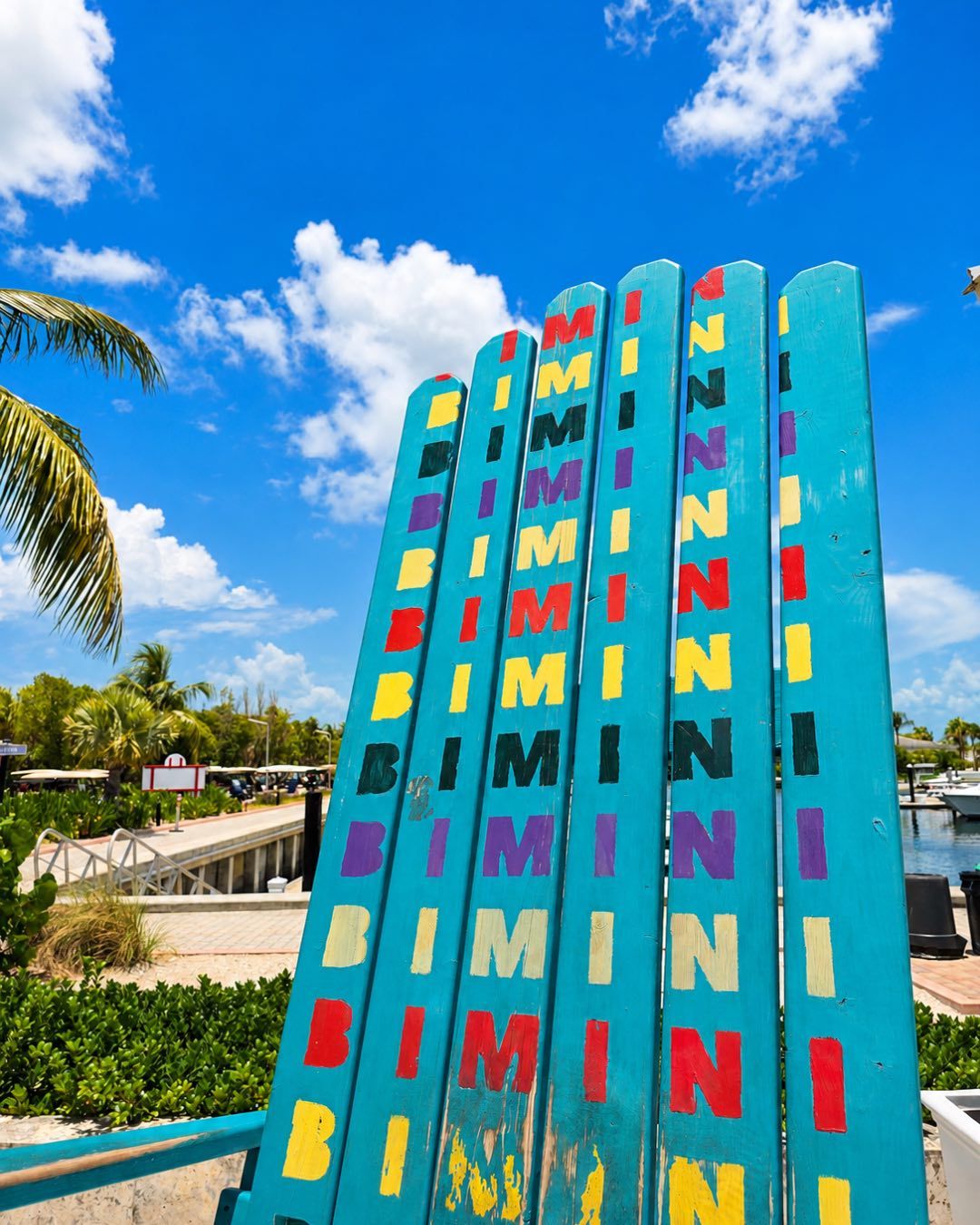 A tall turquoise chair painted with the word Bimini, beside the harbor.